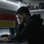 Desenvolvedor de jogos frustrado em frente ao computador com erros de código na tela.